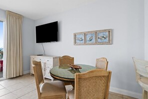Un coin repas comprenant une table ronde en verre, des chaises en bois, un meuble blanc et un téléviseur à écran plat fixé au mur.