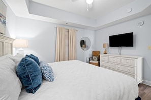 Une chambre à coucher comprenant un lit, une commode, un téléviseur et un ventilateur de plafond.