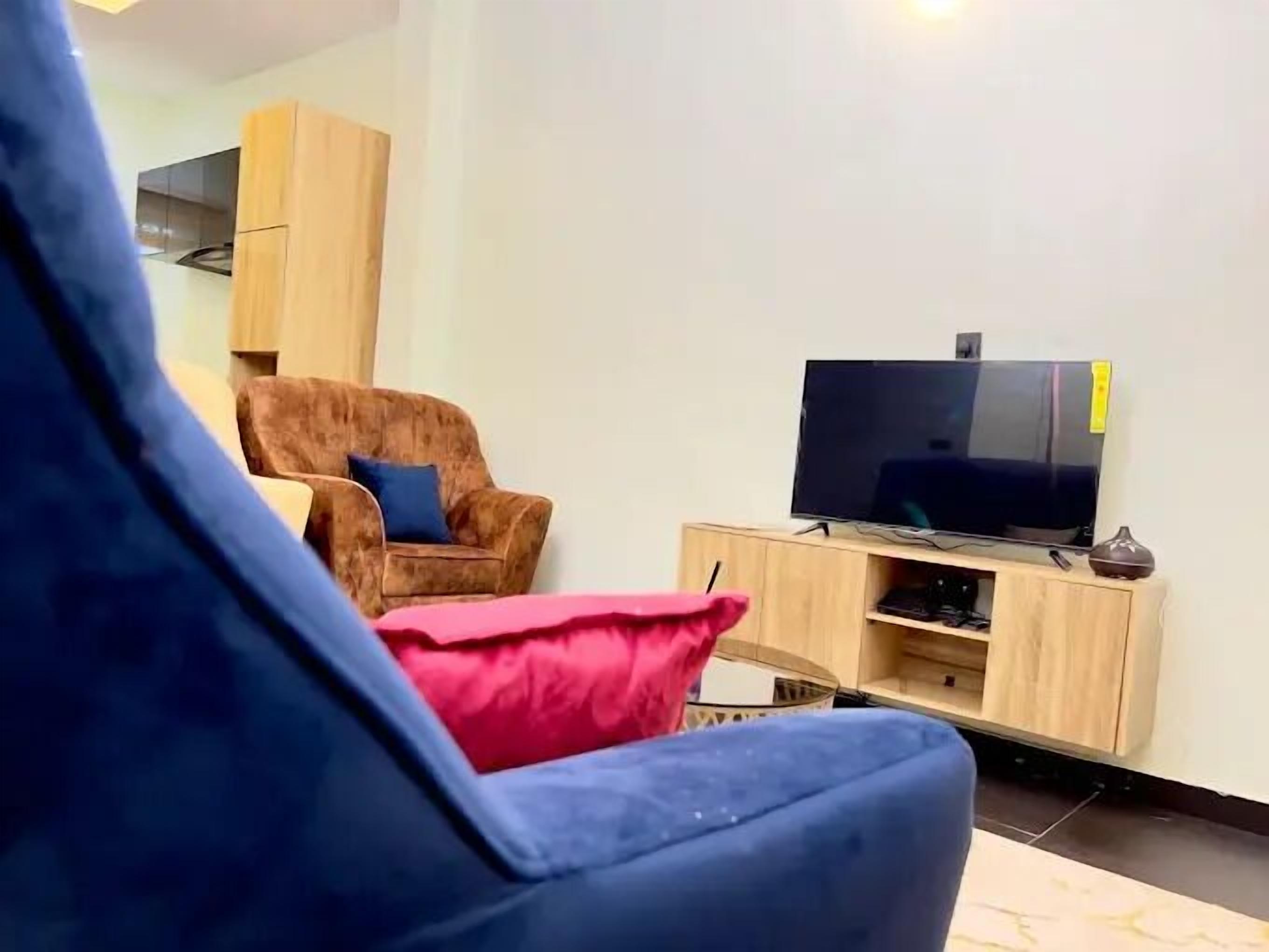 Un salon avec un fauteuil marron, un canapé bleu et un téléviseur posé sur un meuble en bois.