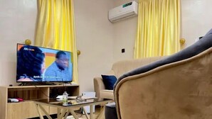 Een woonkamer met een televisie, een bank, een salontafel en gele gordijnen.