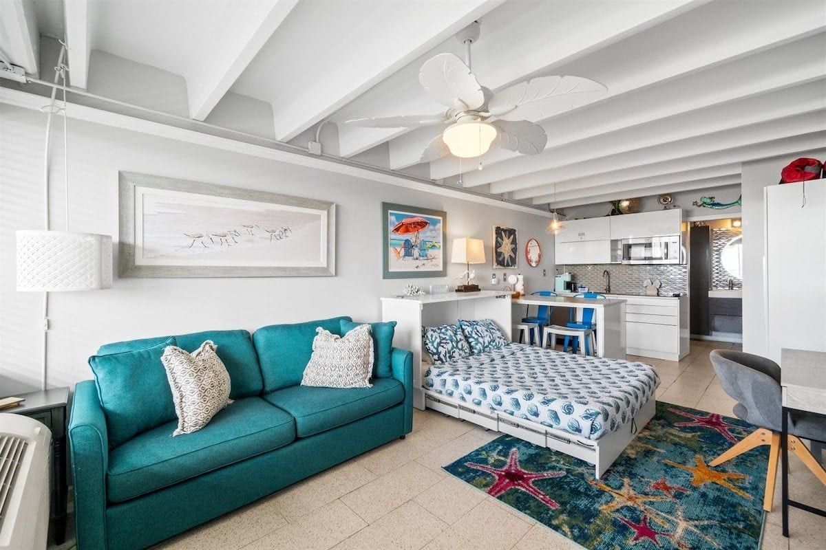 A modern living room with a teal sofa, a bed with patterned bedding, and a starfish rug.