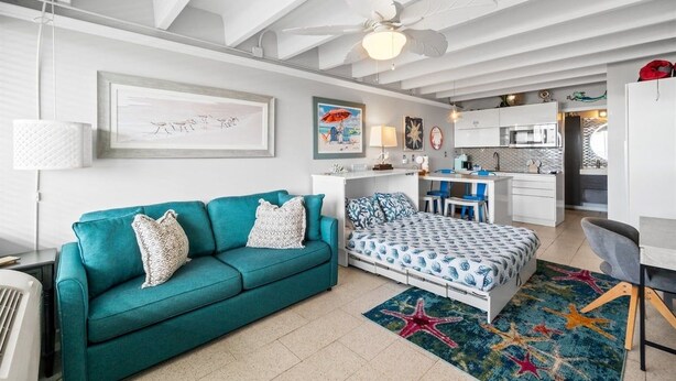A modern living room with a teal sofa, a bed with patterned bedding, and a starfish rug. - Beachfront Studio, Pool (Panama City Beach)