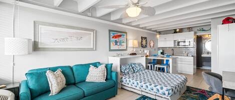 A modern living room with a teal sofa, a bed with patterned bedding, and a starfish rug.
