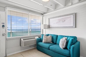 Ein Zimmer mit einem petrolfarbenen Sofa, einem gerahmten Kunstwerk und einem Fenster mit Jalousien.