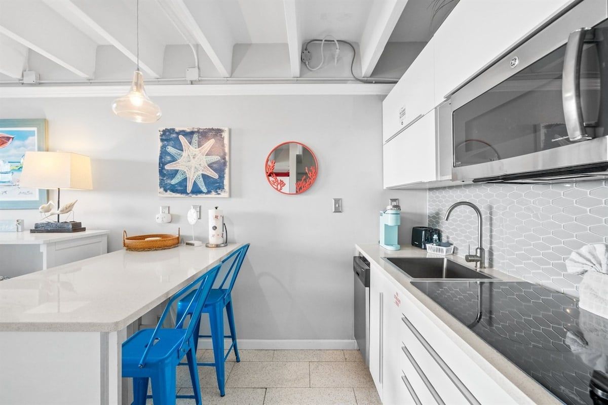 A modern kitchen with a central island, blue bar stools, a stainless steel refrigerator, and a microwave above the counter.