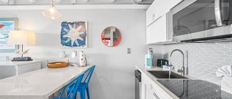 A modern kitchen with a central island, blue bar stools, a stainless steel refrigerator, and a microwave above the counter.