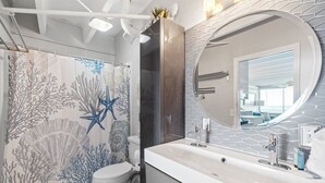A modern bathroom with a shower, toilet, and a large vanity with a mirror. - Beachfront Studio, Pool (Panama City Beach)