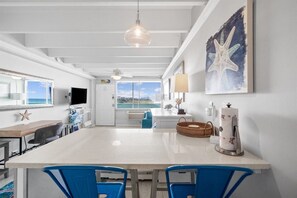 A modern kitchen with a central island, blue chairs, a large window with a view, and a starfish artwork on the wall.