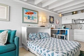 Ein kleines Schlafzimmer mit Bett, Schreibtisch und Kochnische.