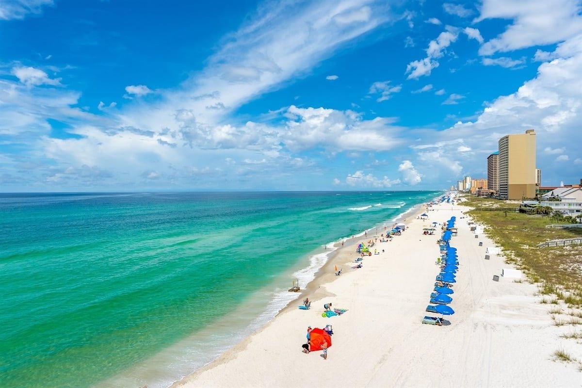 A beach with a clear sky, a sandy shore, and a row of buildings in the background.