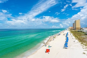 Ein Strand mit blauem Himmel, sandigem Ufer und einer Reihe von Gebäuden im Hintergrund.