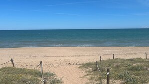 Une plage de sable bordée d’une clôture en bois et où la végétation est clairsemée.