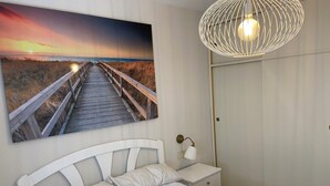 Une chambre à coucher comprenant un lit, une table de chevet, une lampe, une armoire et un tableau représentant un coucher de soleil sur un pont.