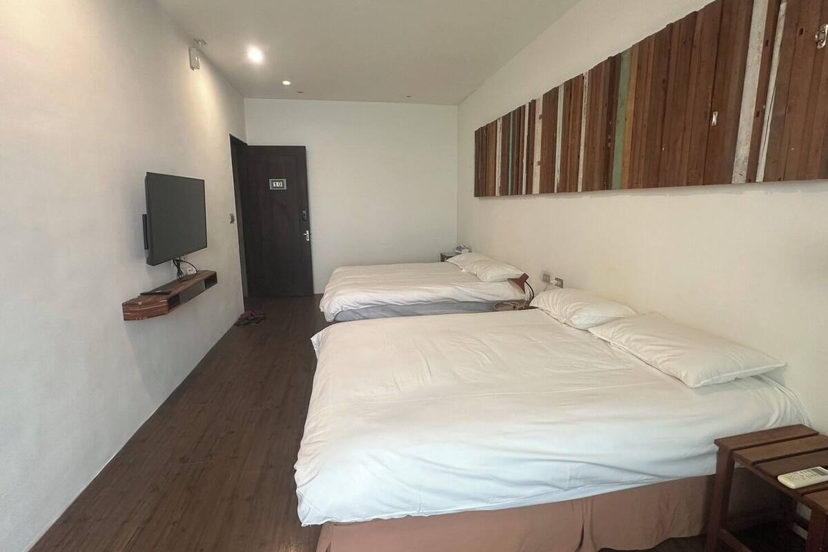 Ein Hotelzimmer mit zwei Betten, einem Fernseher auf einer Holzablage und einer Tür mit einem Schild.