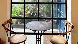 A room with a large window, a round table, two wooden chairs, and a hanging light fixture. - Hour Roots (Tainan)