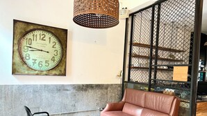 A living room with a vintage clock, a leather sofa, a glass coffee table, and a black chair. - Hour Roots (Tainan)