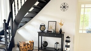 A staircase with black balusters, a wall-mounted compass, a small table with decorative items, a lantern, and a pile of firewood.