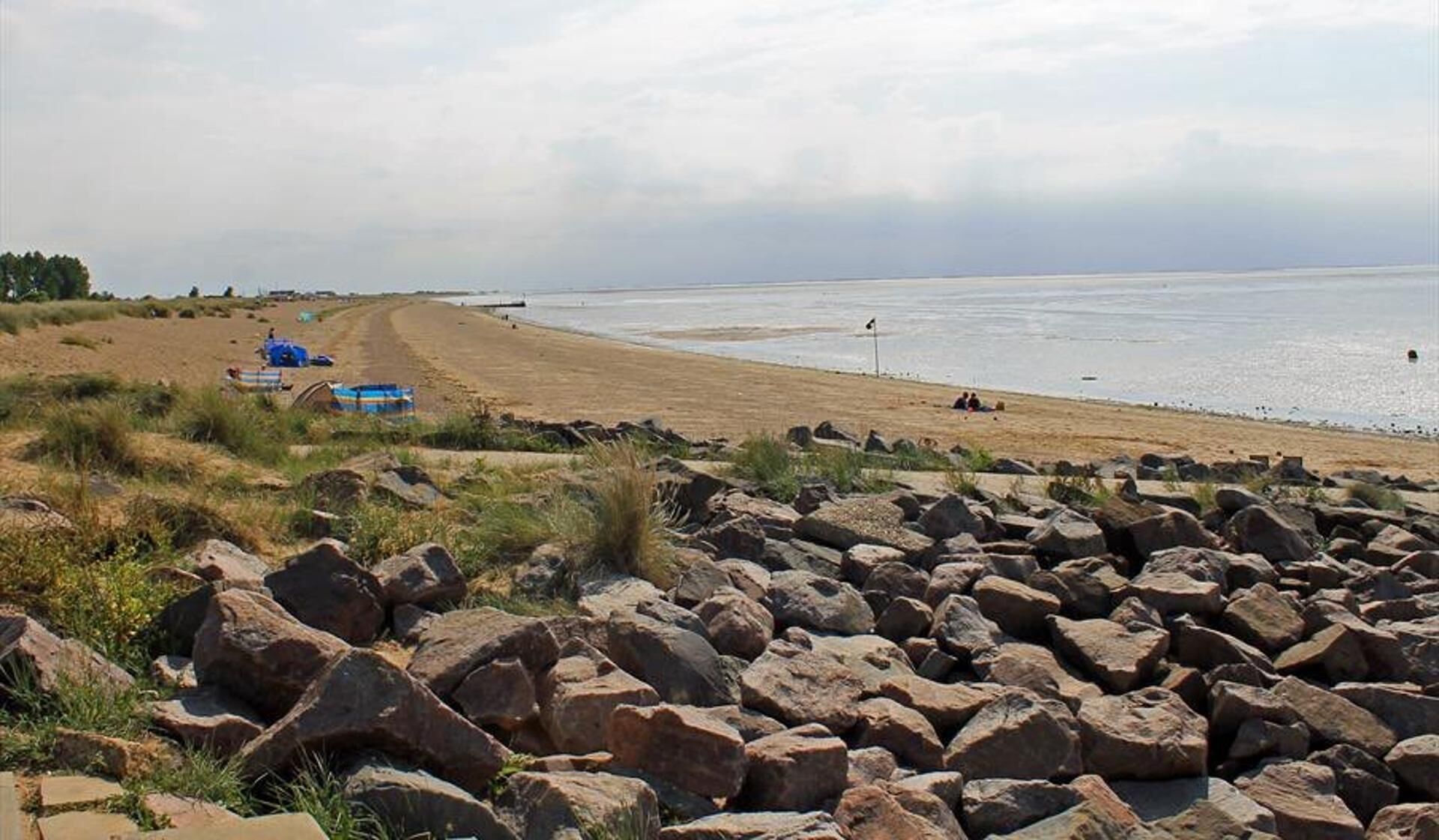 A beach with a rocky foreground, a sandy shore, and a calm sea.
