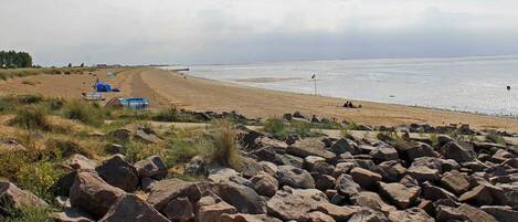 A beach with a rocky foreground, a sandy shore, and a calm sea.