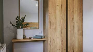 Ein Zimmer mit einem Holzschrank, einem weißen Heizkörper, einem kleinen Tisch mit Topfpflanze und einem Spiegel an der Wand.