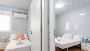 A hotel room with two beds, marble walls, a ceiling fan, and a window with an air conditioning unit.