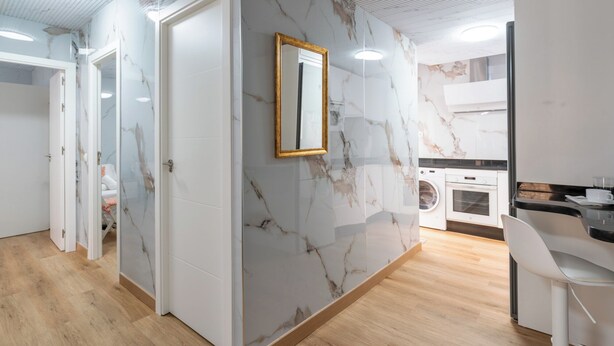 A modern interior with a marble wall, a mirror, and a kitchen area with a washing machine.