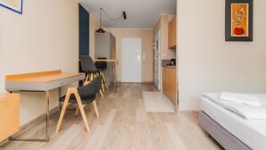 Una habitación compacta con cama, escritorio, silla, kitchenette y puerta.