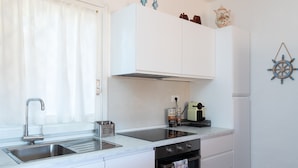 A modern kitchen with white cabinetry, a stainless steel sink, an induction cooktop, and a built-in oven. - Casa Cerbiatta al Molo 2 by Wonderful Italy (Arzachena)