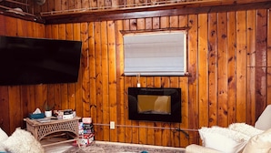 Een gezellige woonkamer met houten wanden, een flatscreen televisie, een bank en een fauteuil.