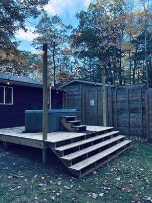 A wooden deck with steps leading to a hot tub, surrounded by a wooden fence and trees.