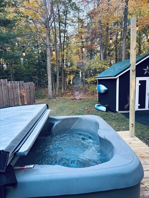 Un jacuzzi dans un jardin, avec une terrasse en bois, un abri de jardin et des arbres en arrière-plan.