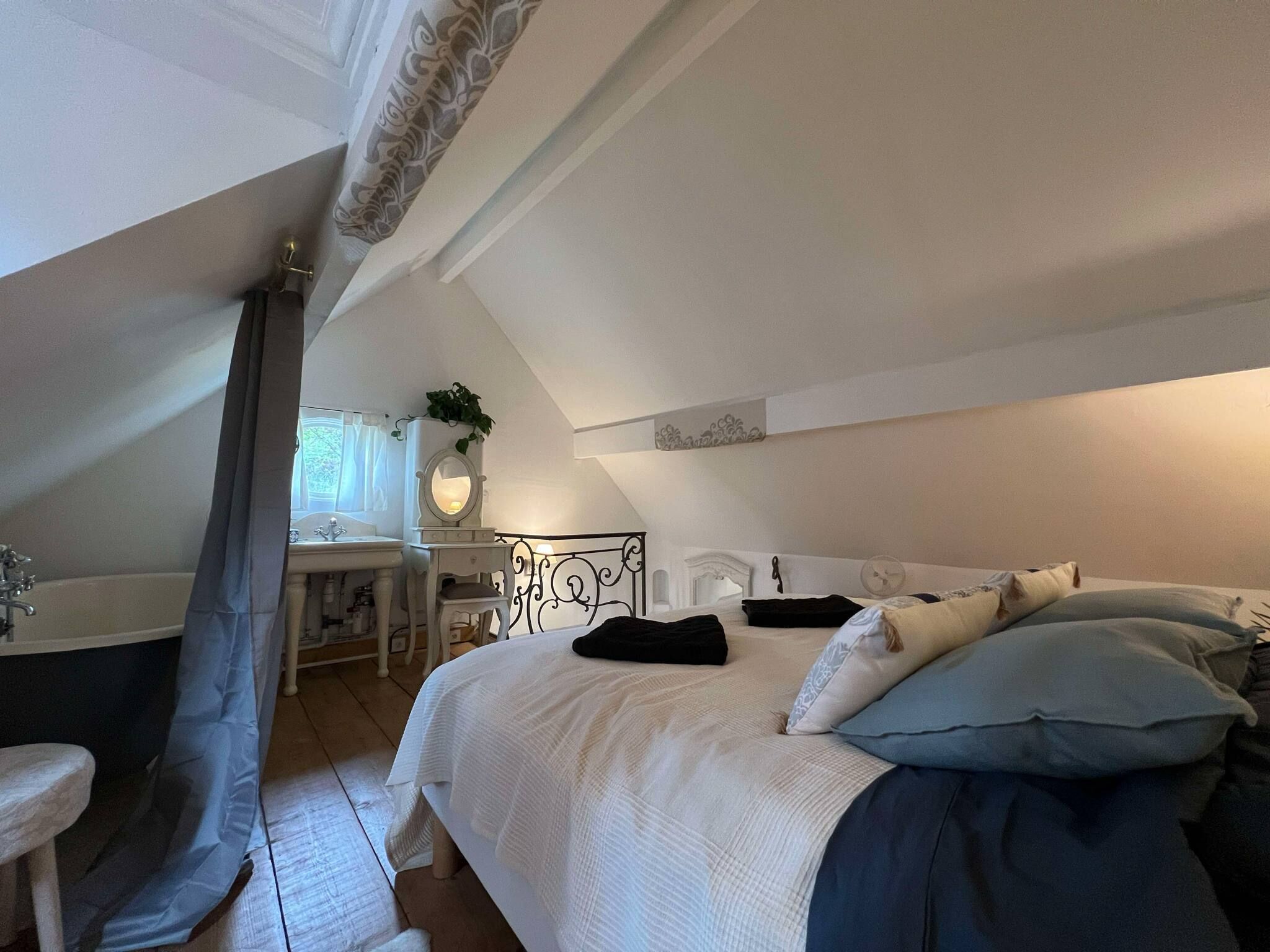 Une chambre à coucher avec un lit, une table de chevet, une commode, un miroir et une fenêtre avec des rideaux.