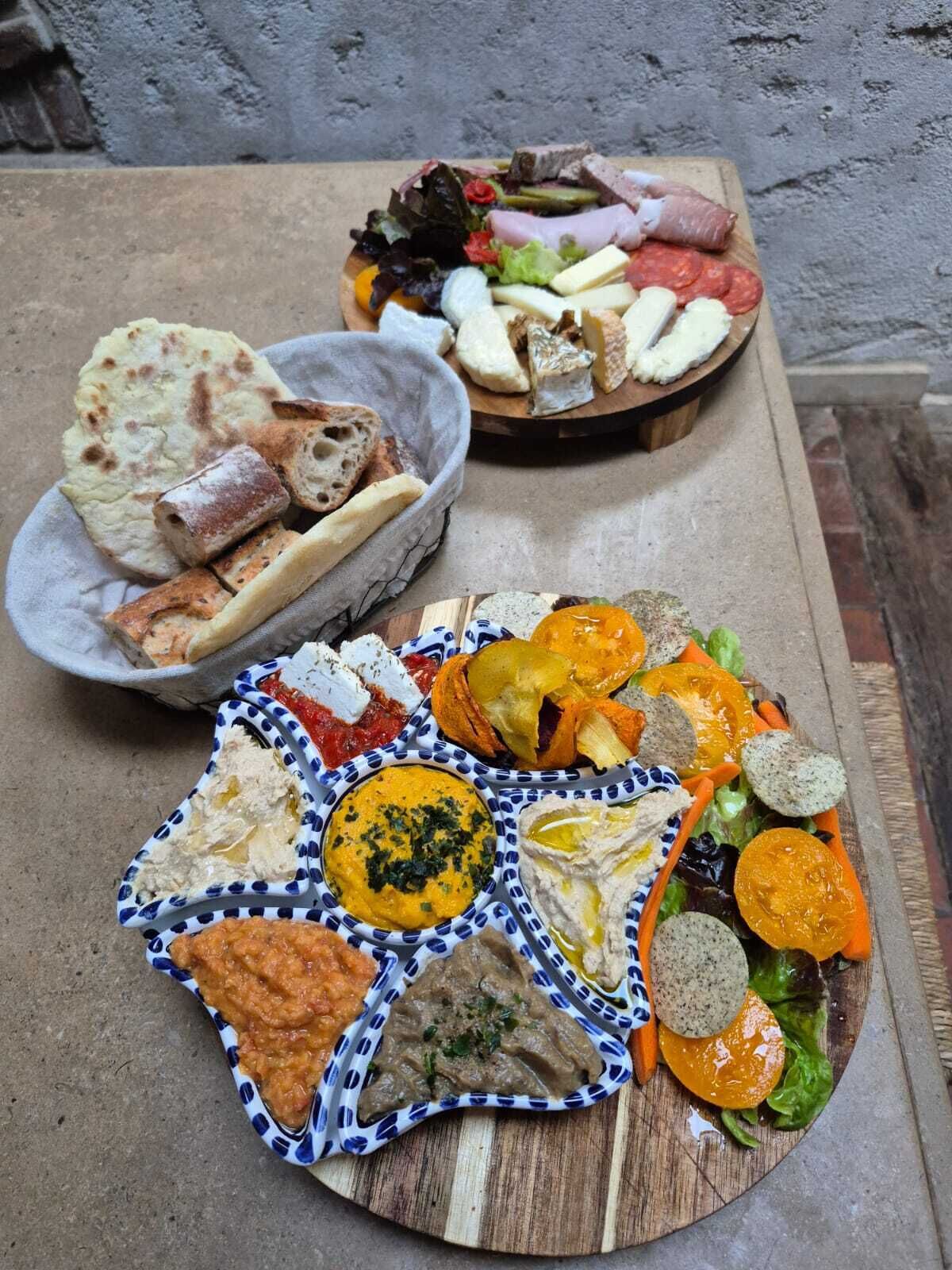 Ett urval av matvaror, inklusive tunnbröd, ostar, kött och dippsåser, upplagt på ett träbord.