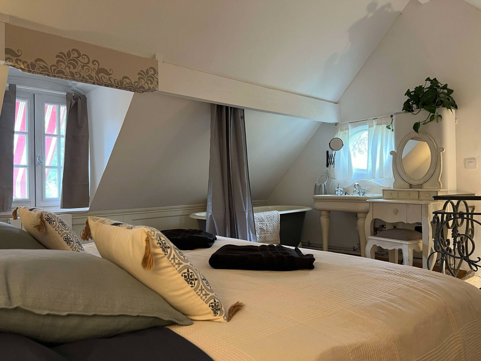 A bedroom with a large bed, a vanity with a mirror, a plant, and a window with curtains.