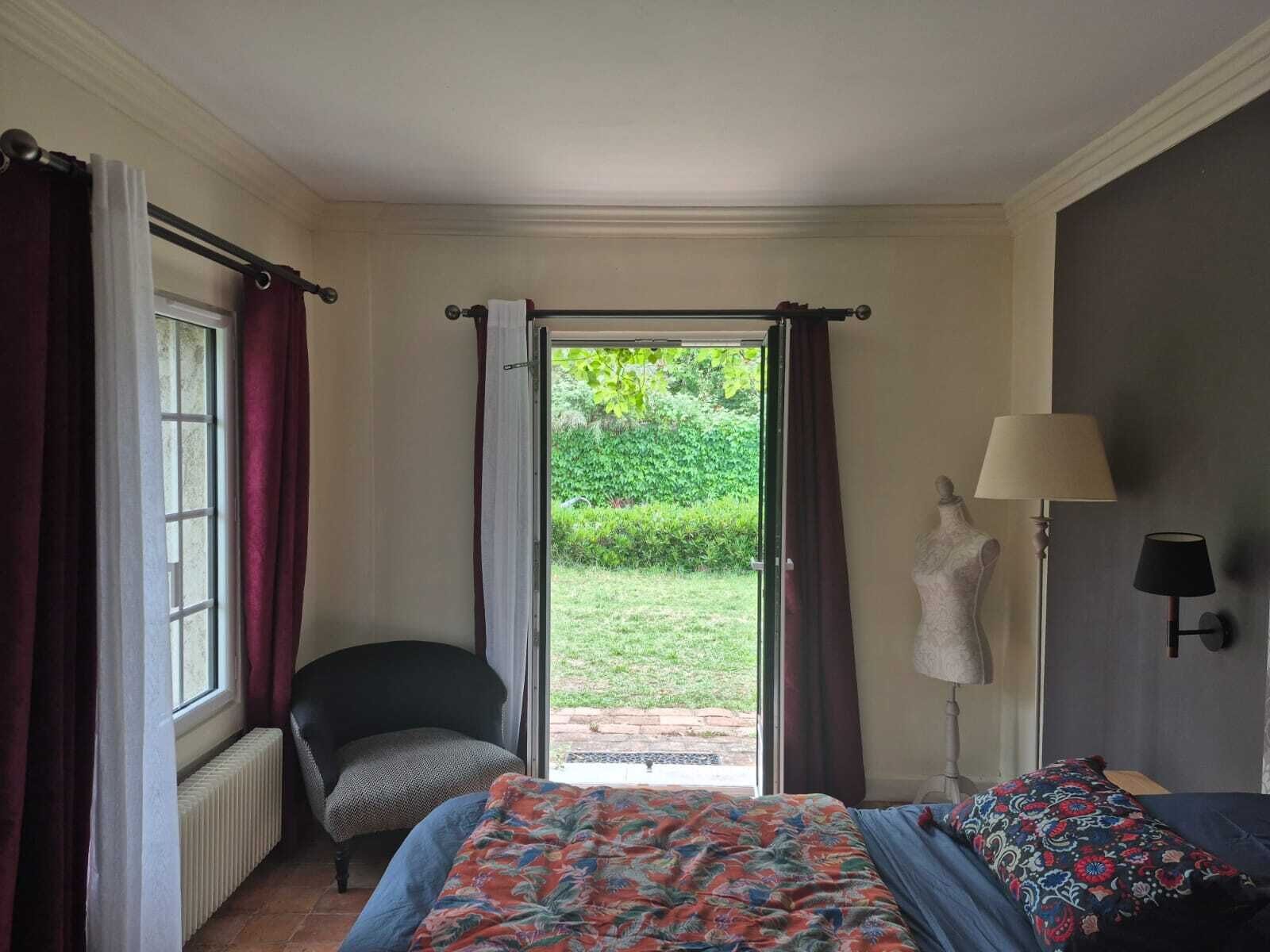 A bedroom with a bed, a chair, a radiator, a lamp, and a view of a garden through a sliding door.