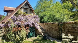 A rustic house with a steeply pitched roof, a stone wall, and a green gate.