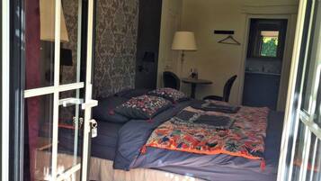 Un dormitorio con cama, una silla, una mesa y una lámpara. Hay una ventana y una puerta.