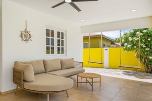 Una habitación con un sofá curvo, una mesita, un ventilador de techo, una ventana y una pared amarilla con un columpio.