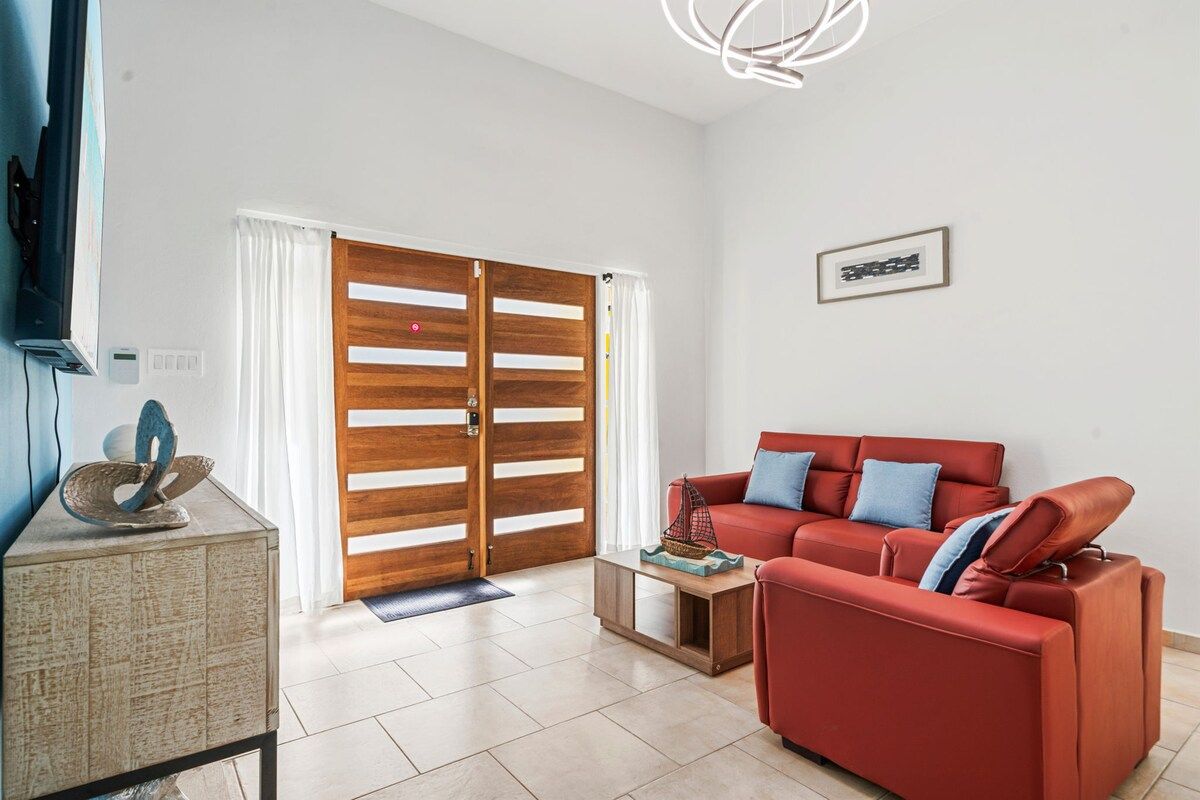 A living room with a red sofa, a wooden door, and a framed picture on the wall.