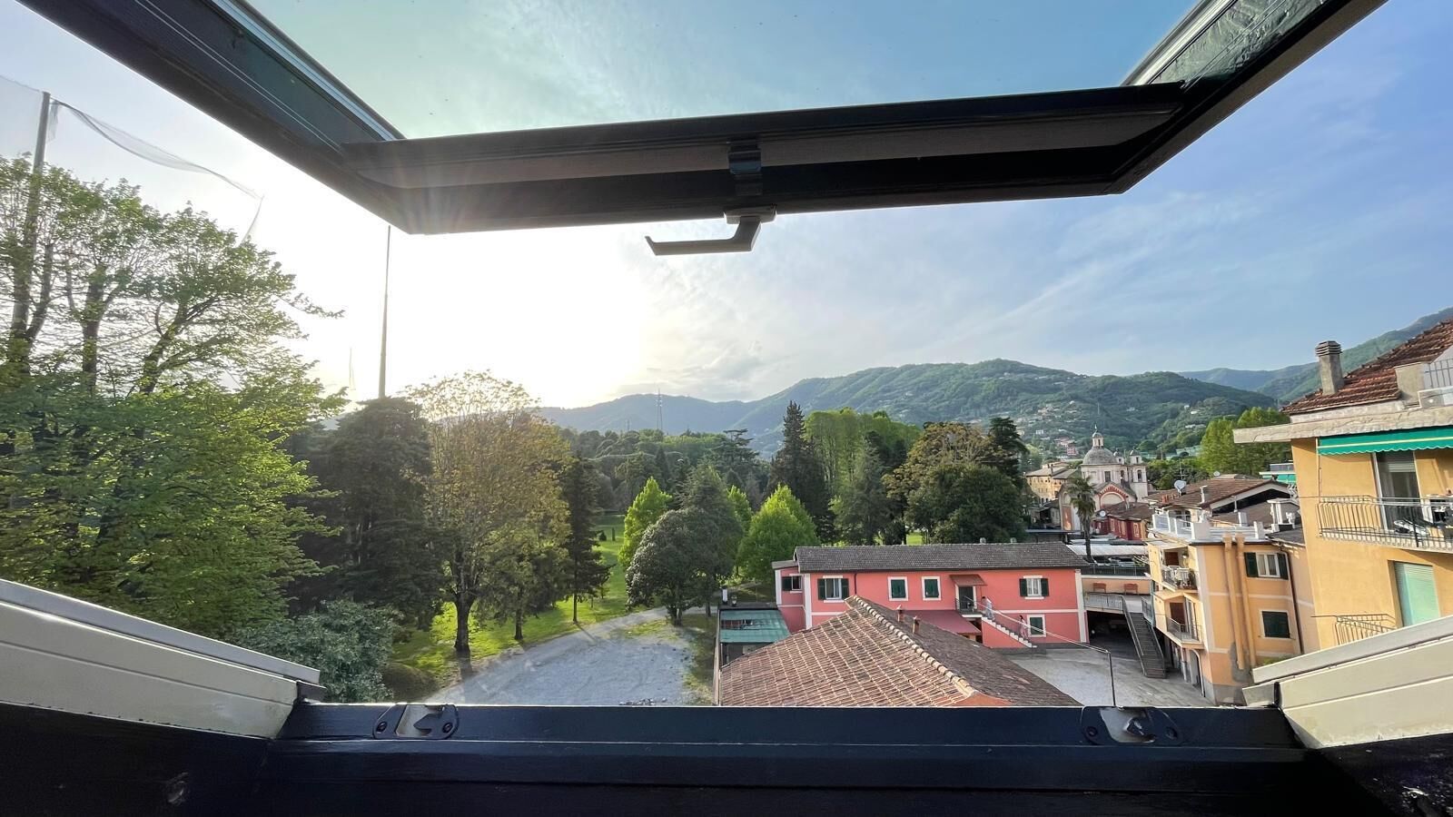 A view from a window overlooking a town with buildings, trees, and mountains in the background.