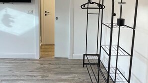 Een kamer met een houten vloer, een aan de muur bevestigde televisie, een deur en een metalen rek.