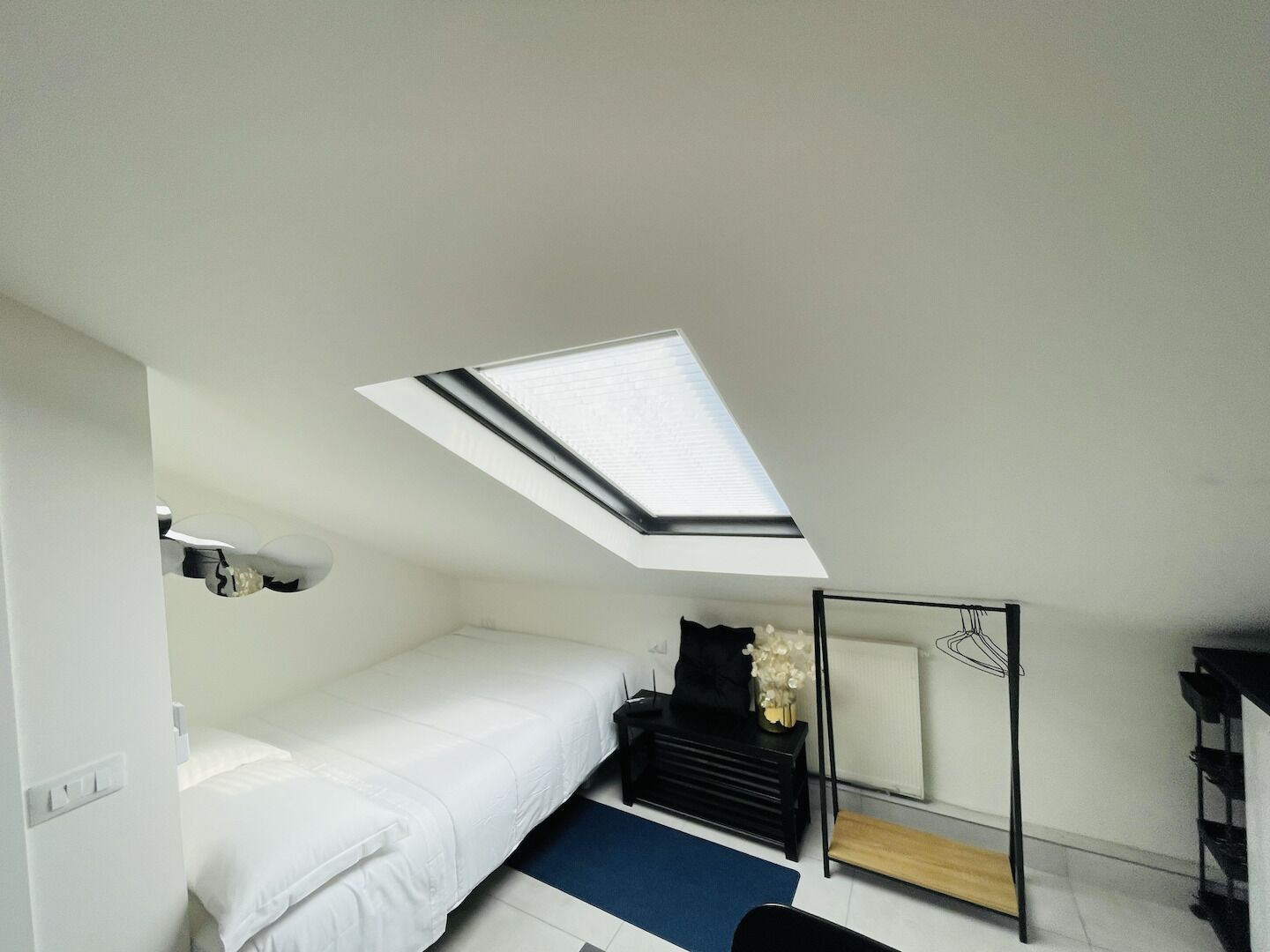 A compact hotel room with a skylight, a bed, a desk, and a chair.