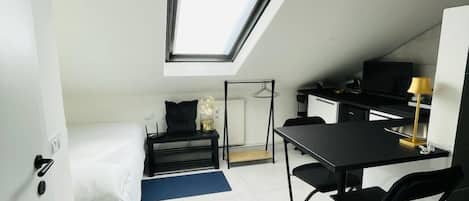 Quarto compacto com claraboia, cama, escrivaninha e cadeira.