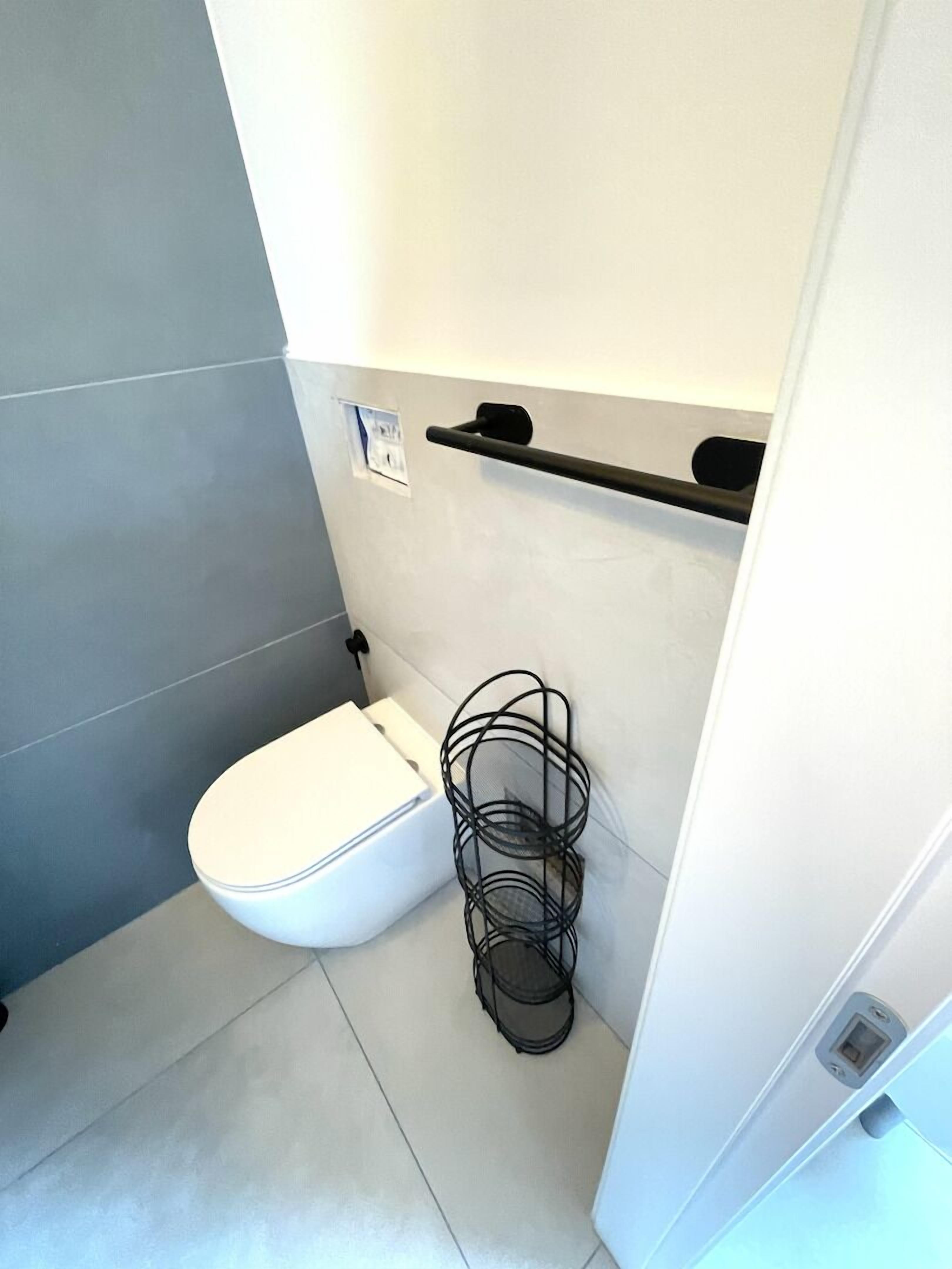 Un baño moderno con inodoro blanco, baldosas grises y estante de metal negro.