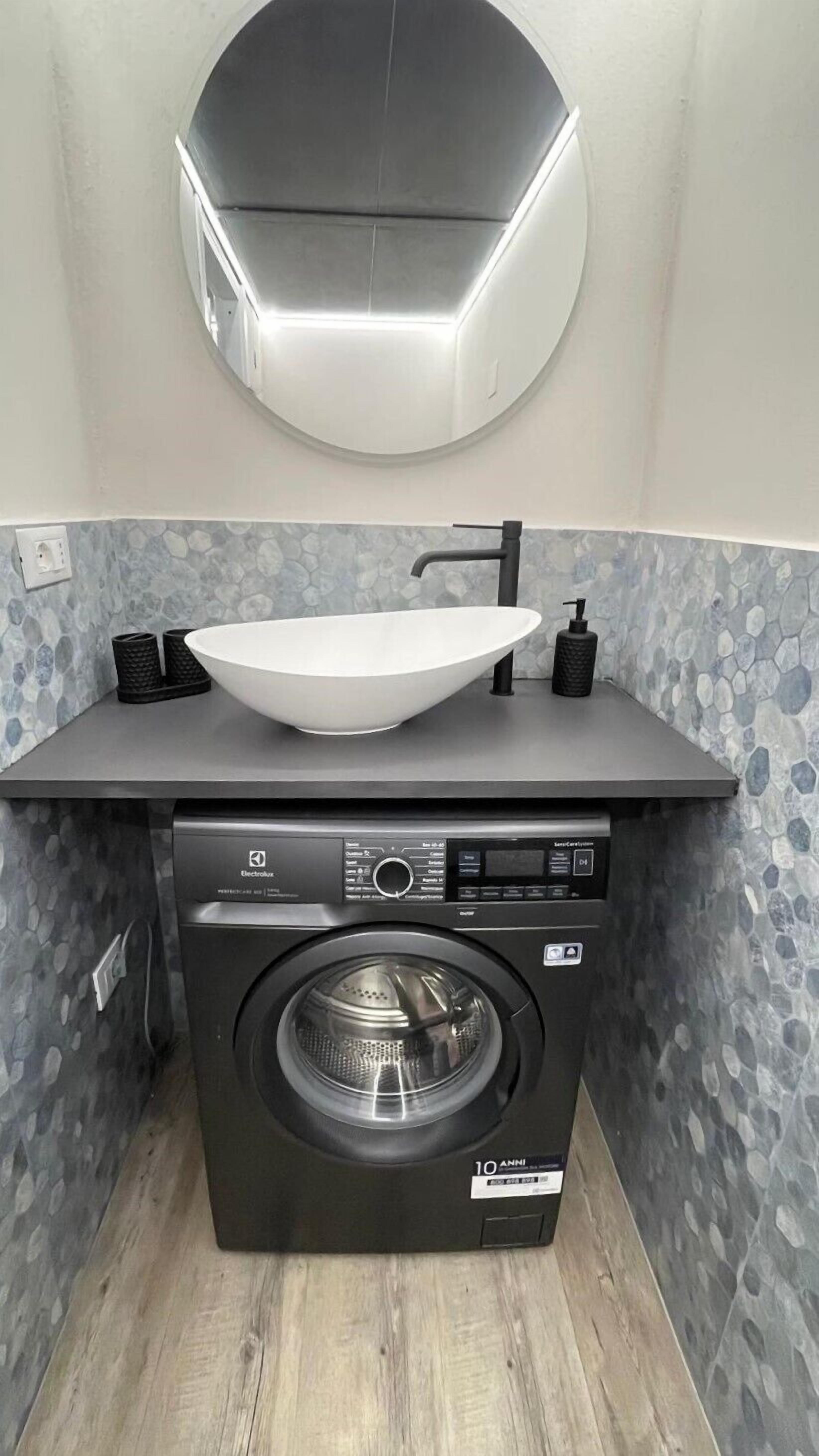 Lavadora compacta y lavamanos en un baño pequeño con salpicadero decorado con un diseño de piedra.
