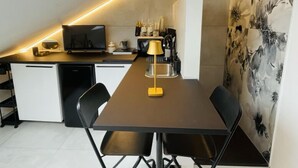 Een moderne keuken met een eethoek, met een lange tafel, zwarte stoelen, een gele lamp en een plafondlamp.