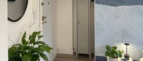 A hallway with a white console table, a potted plant, a mirror, and a coat rack. There is a door with a coat hanging on it.