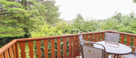 Une terrasse en bois avec une table et des chaises en métal, entourée d’une balustrade en bois ornée de motifs découpés.