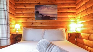 Une chambre rustique en bois, avec un lit, deux lampes de chevet et un tableau encadré au mur.