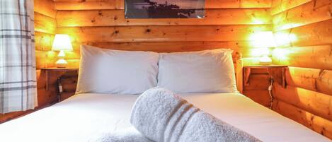 A wooden cabin room with a bed, two bedside lamps, and a framed picture on the wall.